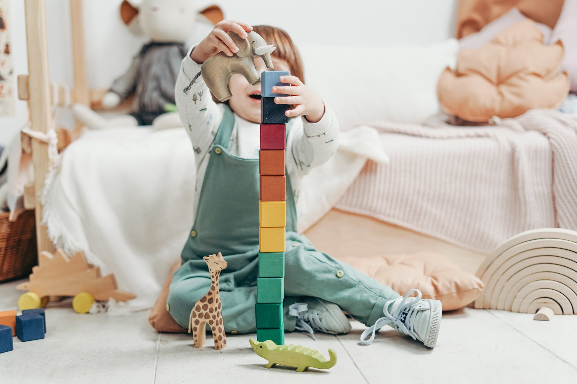 child in green and white long sleeve top and dungaree trousers holding blue and yellow lego blocks